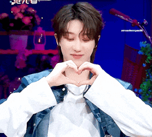 a man is making a heart shape with his hands and the words strawberrymilk are visible behind him