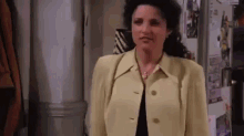 a woman in a yellow jacket is standing in front of a refrigerator in a room .