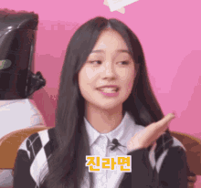a girl with long black hair is sitting in front of a pink background with chinese writing