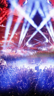 a crowd of people at a concert with blue and red lights coming from the stage