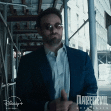 a man in a suit and sunglasses is standing in front of a sign that says daredevil born again .
