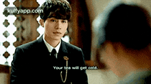 a man in a suit and tie is talking to another man and says your tea will get cold .