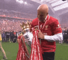 a man in a red shirt is holding a trophy that says ' premier league ' on it