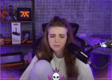 a woman sitting in front of a shure microphone with a skull necklace
