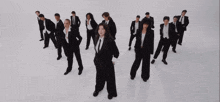 a group of people in suits and ties are standing in a row on a white surface .