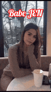 a woman sits at a table with a cup of coffee and the words babe jen on the bottom