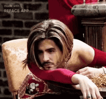 a man with long hair and a beard is sitting in a chair with his head on his arm .