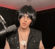 a man is standing in front of a microphone wearing a wig and a necklace .