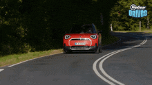 a red mini cooper driving down a road with topgear drive written on the bottom
