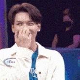 a man in a white jacket is covering his face with his hand while smiling .