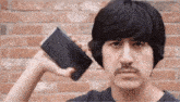 a man with a mustache is holding a cell phone in front of his ear .