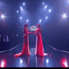 two women in long red dresses are holding hands on a stage