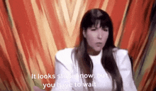 a woman is sitting in front of a red curtain and says `` it looks stupid now , but you have to wait ''