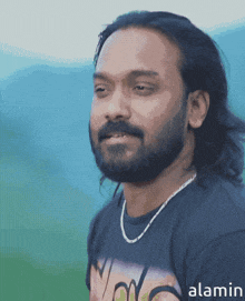 a man with long hair and a beard is wearing a t-shirt with the word alamin on the bottom