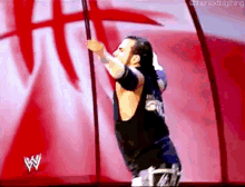 a wrestler is holding a pole in front of a red background with the letter w on it .