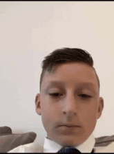 a young boy wearing a white shirt and tie looks at the camera with his eyes closed