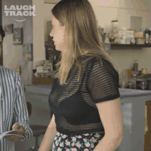 a woman in a black top is standing next to a man in a striped shirt with the words laugh track behind her
