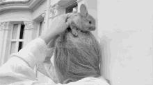 a black and white photo of a woman petting a small mouse on her head .