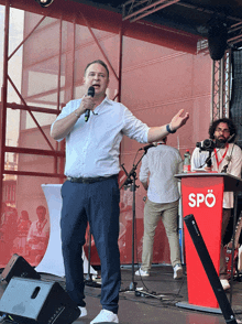 a man speaking into a microphone in front of a red podium that says spo