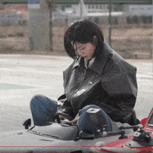 a woman wearing a black jacket is sitting on a car