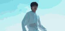 a young man wearing a necklace and a white shirt is standing in front of a blue sky