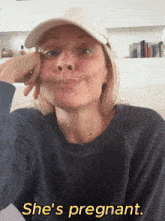 a woman wearing a hat says she 's pregnant in yellow letters