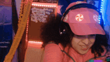 a woman wearing headphones and a pink hat is smiling in front of a halloween sign