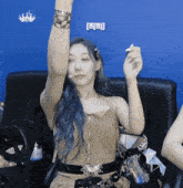 a woman with blue hair is sitting in a chair with her arm up