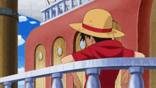a man wearing a straw hat and a red shirt is standing on a balcony