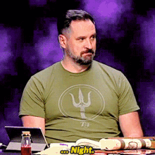 a man wearing a green t-shirt with the letter w on it sits at a table