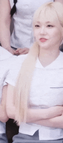 a girl with long blonde hair is sitting with her arms crossed in front of a group of people .
