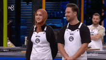 a man and a woman standing next to each other wearing aprons with the letter m on them