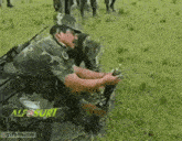 a man in a camouflage uniform is kneeling down in a field with a gifbin.com watermark