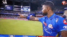 a man in a blue shirt is pointing at something on a cricket field