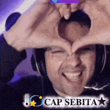a man wearing headphones is making a heart with his hands in front of his face