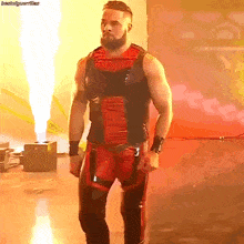 a wrestler in a red and black outfit is walking in front of a fire