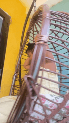 a woman in a yellow dress is sitting in a wicker hanging chair