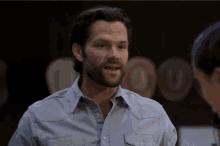 a man with a beard wearing a light blue shirt is talking to a woman