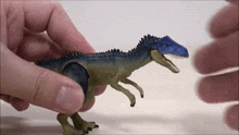 a person is holding a toy dinosaur with a blue head and blue teeth .
