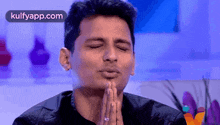 a man in a black shirt is praying with his eyes closed