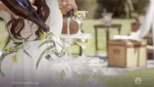 a woman is pouring champagne into a pyramid of glasses .