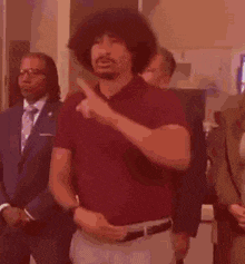 a man with a beard and curly hair is standing in a room with other men .