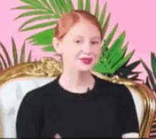 a woman is sitting in a chair with a pink background and palm leaves behind her .