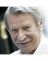 a man with gray hair and a mustache is smiling and looking at the camera