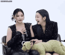 two women are sitting next to each other with a stuffed animal between them .