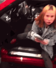 a girl is getting out of a red car while holding a cell phone