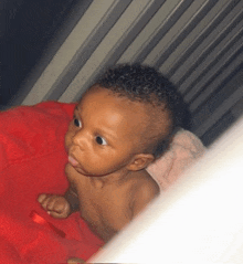 a baby is laying on a red blanket in a crib and looking at the camera