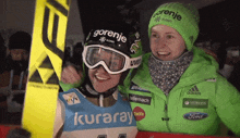 a woman wearing a gorenje helmet stands next to a woman wearing a kuraray jacket