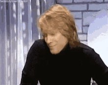 a close up of a man with long hair wearing a black turtleneck sweater .