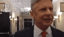 a man in a suit and tie is standing in a hallway talking to someone .